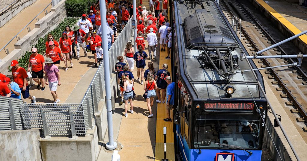 Cardinals fans arrive at Stadium MetroLink Station from a blue light rail vehicle.